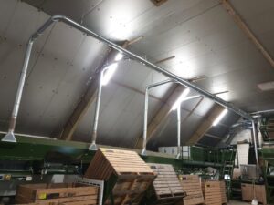 Metal extraction arms and hoods mounted above a long potato sorting belt in an agricultural shed.