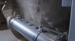 Nahaufnahme eines metallenen Saugrohrs, das Staub von Jutesäcken mit Kartoffelfüllung absaugt.