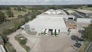 Vue aérienne du site industriel de Groka avec ses grands halls de production, ses camions à quai et les champs agricoles environnants.