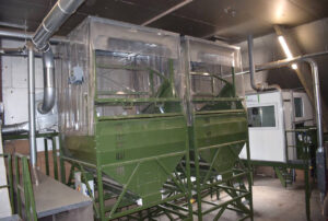 Two large green dust collection units with transparent covers and connected extraction ducts in the sorting area of De Lugt.