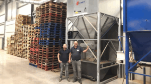 Zwei Mitarbeiter an einer großen Staubabsauganlage der Firma Jongejans Luchttechniek, umgeben von gestapelten Paletten.