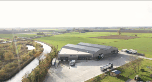 Drohnenaufnahmen des Geländes von Aardappelhandel Mol in einer ländlichen Gegend, mit Schuppen, Lastwagen und umliegenden landwirtschaftlichen Feldern.