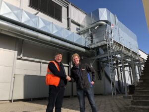 Two employees at AWEX in front of the outdoor installation of the chain filter system from Jongejans Luchttechniek, which extracts dust, skins and sealing fumes.